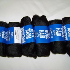 four rolls of black wool sitting next to each other on a white tableclothed surface