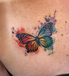 a colorful butterfly tattoo on the back of a woman's left shoulder and chest