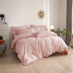 a bed with pink sheets and pillows in a white room next to a large window