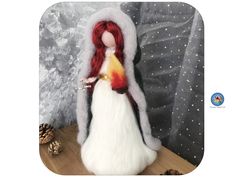 a doll with red hair and white dress is standing on a wooden table next to pine cones