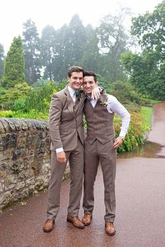 two men standing next to each other wearing suits and ties with trees in the background