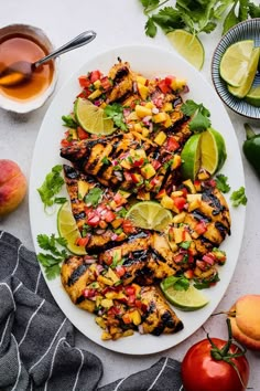 grilled chicken with mango salsa on a white plate next to sliced peaches and limes