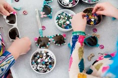 two women are making beaded sunglasses at a table with other beads and accessories on it