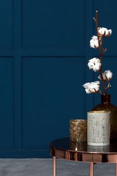 a vase with cotton flowers sitting on top of a table next to a candle holder