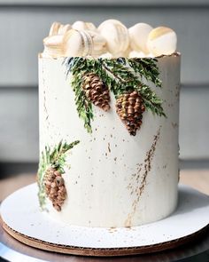 a white cake decorated with pine cones and evergreen leaves