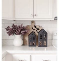 two small houses are sitting on the kitchen counter next to a vase with flowers in it