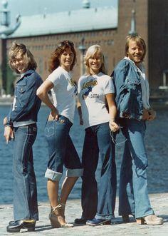 four people standing next to each other near the water