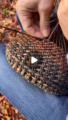 a person is holding an object in their hand while sitting on the ground with autumn leaves around them