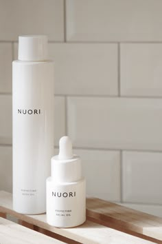 two white bottles sitting next to each other on a wooden shelf in front of a tiled wall