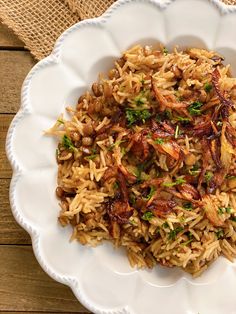 a white bowl filled with rice and meat on top of a wooden table next to a burloom cloth