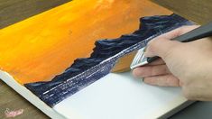 a person using a pen to paint an orange and blue painting on a piece of paper