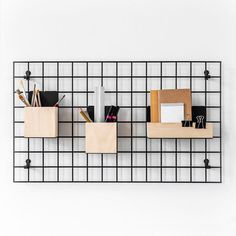 three wooden boxes with pens, pencils and other office supplies on a metal grid wall