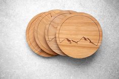 four wooden coasters with mountains engraved on the front and back, sitting on a gray surface