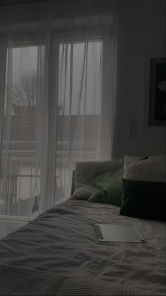 a laptop computer sitting on top of a bed next to a window with sheer curtains