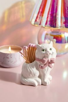 a white cat figurine next to a lit candle on a pink counter top