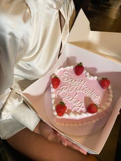 a heart shaped cake with strawberries on top is being held by a woman in a white dress