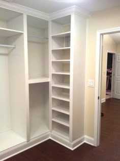 an empty walk in closet with white shelving and wood flooring on the side