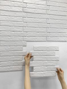 two hands are holding up a white brick wall with the bricks on it's sides