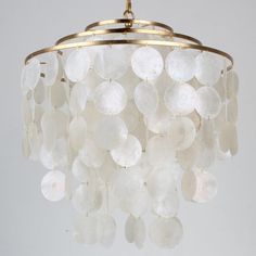 a chandelier made out of white shells hanging from a ceiling fixture with gold trim