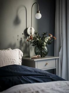 a vase with flowers sitting on top of a bed next to a night stand and lamp