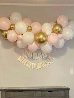 balloons and streamers are hanging from the ceiling above a dresser in a room with white walls