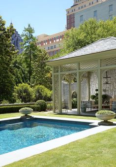 a gazebo in the middle of a lawn with a pool and seating area next to it