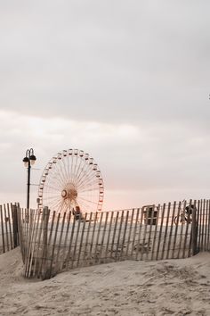 a ferris wheel sitting on top of a sandy beach next to a wooden picket fence