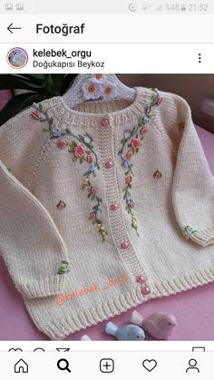 a knitted sweater with flowers and leaves on the front, sitting on top of a pink table