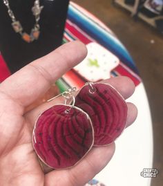 a person holding two heart shaped earrings in their hand with other items on the table behind them