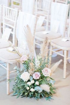 an arrangement of flowers and feathers sits on the floor in front of chairs at a wedding