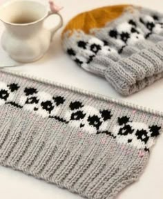 two knitted mittens sitting on top of a table next to a coffee cup