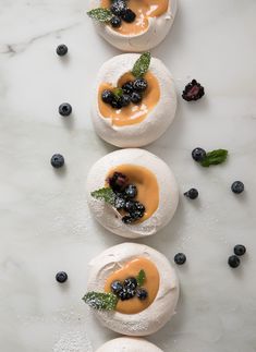 three small pastries with blueberries and mint on them are sitting on a white surface