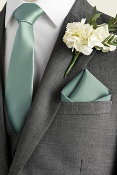 a man wearing a gray suit with a green tie and flower boutonniere