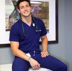 a male in a blue scrub suit sitting on top of a white stool with a stethoscope