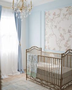 a baby's crib in front of a chandelier and curtained window