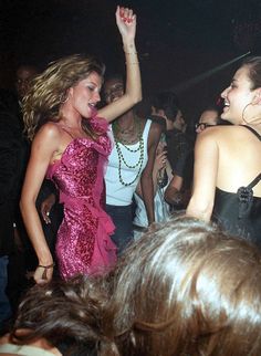 two women dancing at a party with other people in the back ground and one woman holding her hand up