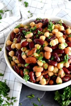 a white bowl filled with beans and parsley on top of a table next to napkins