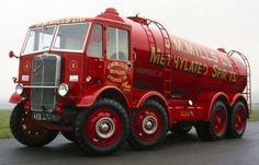 a red cement mixer truck driving down a road next to a grass covered field in the background