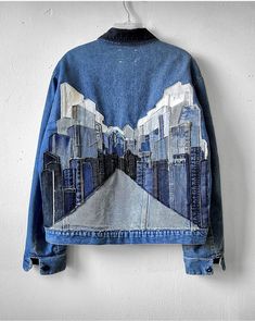 a denim jacket with an image of a city on it hanging from a hook in a white wall