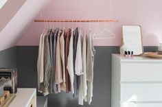 an organized closet with clothes hanging on the rail and drawers in front of it, under a slanted ceiling