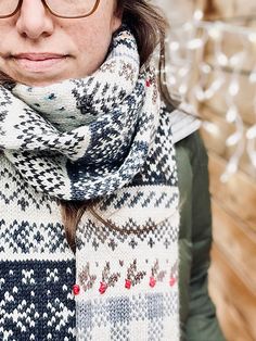 a woman wearing glasses and a scarf is standing in front of a wall with christmas lights