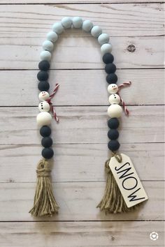 the snowman beaded necklace is hanging on a white wooden wall with a tag