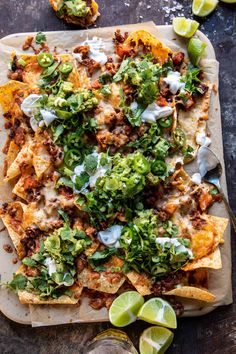 nachos with meat, cheese and salsa on a cutting board next to lime wedges