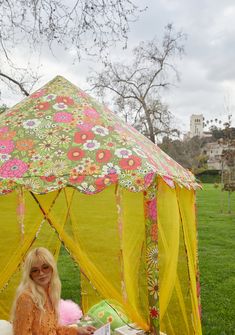 a woman sitting in front of a yellow tent on top of a lush green field