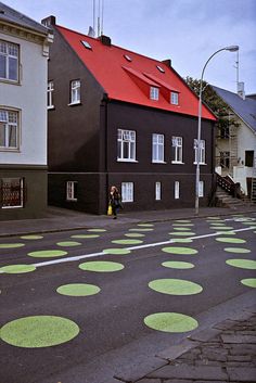 an empty street with green circles painted on the pavement and houses in the background,