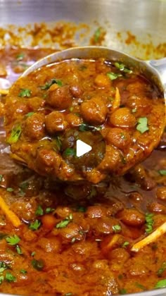 a ladle full of meat and vegetables being stirred by a spoon in a pot