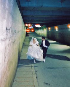 a bride and groom are walking down the street in their wedding gowns, under an overpass