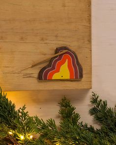 a piece of wood is hanging on the wall next to some christmas tree branches and lights