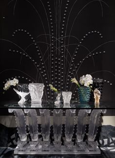 glass vases and flowers sit on a table in front of a black wall with an intricate design