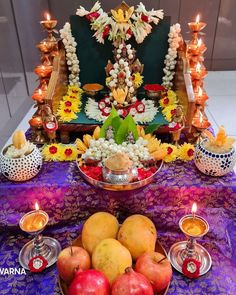 an arrangement of fruits and candles on a table in front of a decorated statue with flowers